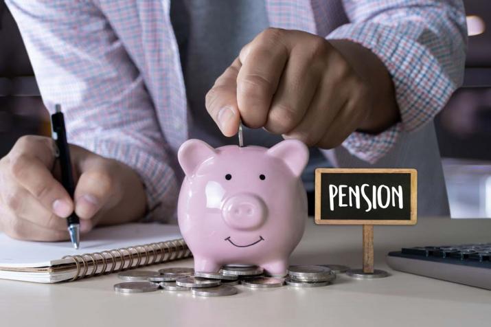 Pensions: a man drops coins in a piggy bank for his future pension, while calculating his expenses Pensions: a man drops coins in a piggy bank for his future pension, while calculating his expenses